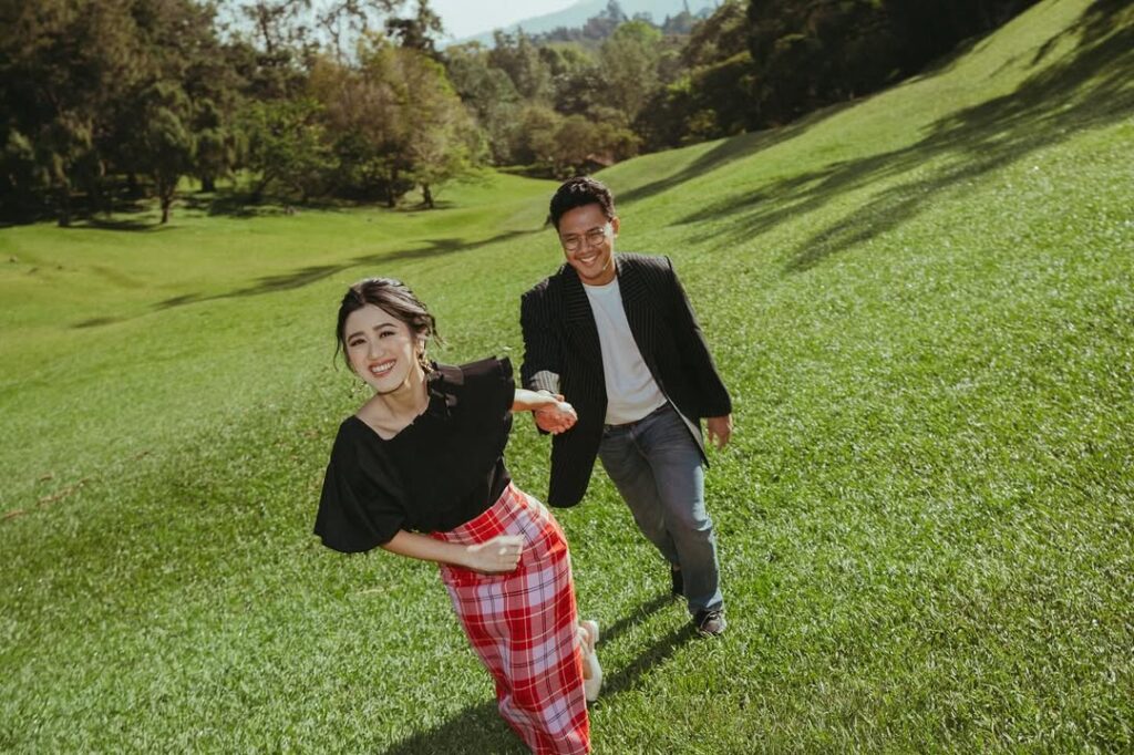 Pasangan prewed berlarian dan tertawa di atas rumput hijau Kebun Raya Cibodas. source: sabilasyarafina